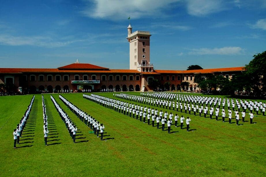 Formatura de cadetes no gramado da EsPCEx, em Campinas, em frente ao prédio histórico com torre, em dia de céu azul.